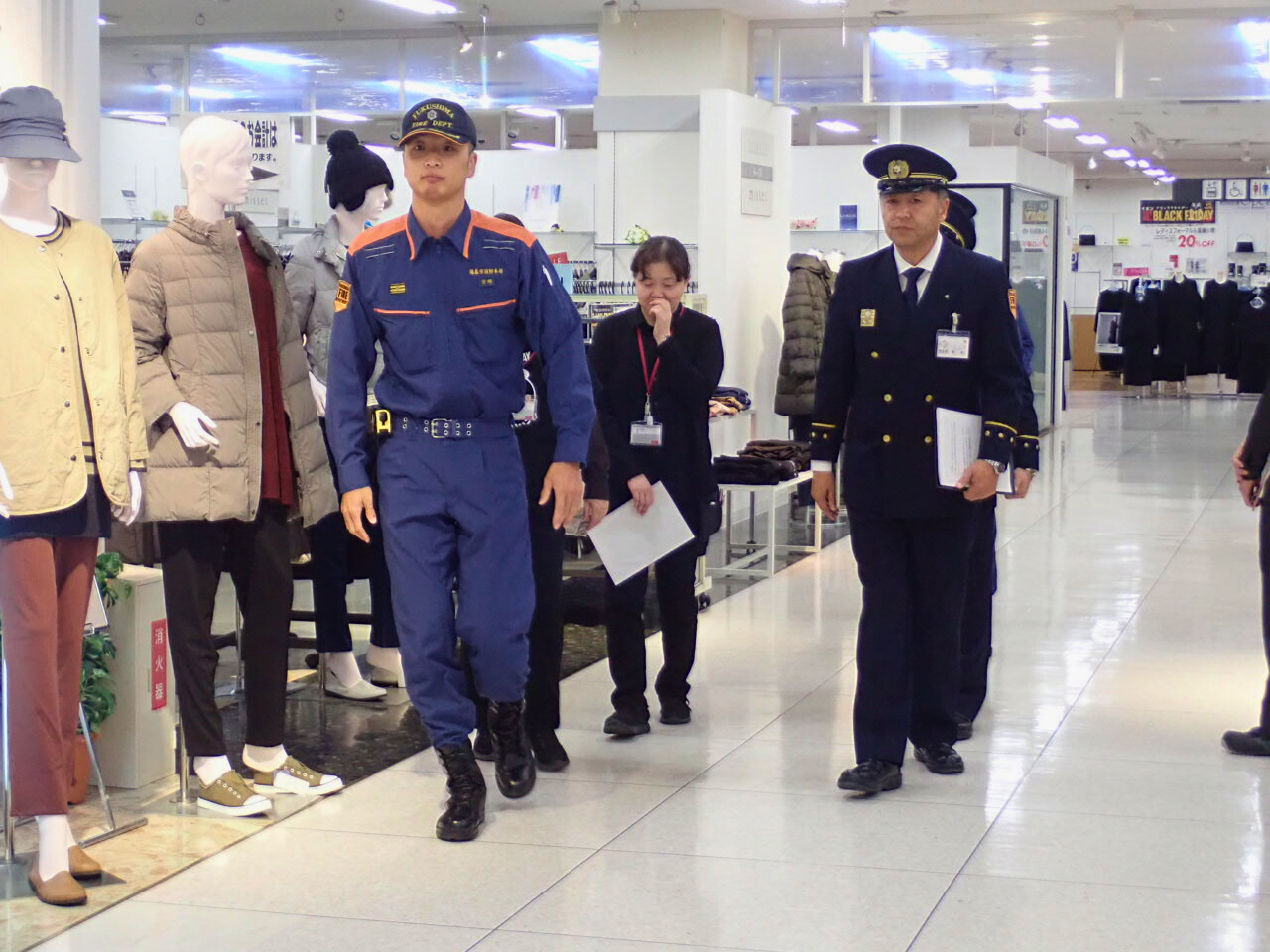 福島市消防長と検査担当職員が、商業施設従業員とともに店内を検査して回っている様子