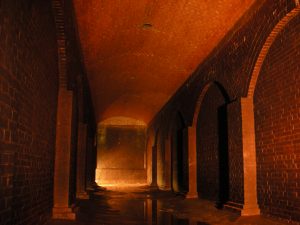 重厚な煉瓦造りの壁とアーチ、そして半円形のヴォールト天井で構成された、長い地下通路のような空間の写真