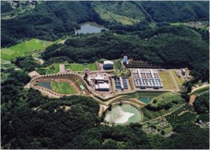 緑色に生い茂った森といくつかの調整池に囲まれた、広大な敷地内に多数の沈殿槽や処理施設が整然と配置されたすりかみ浄水場を上空からとらえた写真