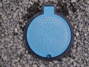 地面に設置された青色の円形の蓋に「水抜栓」と書かれた水抜栓を拡大で撮影した写真