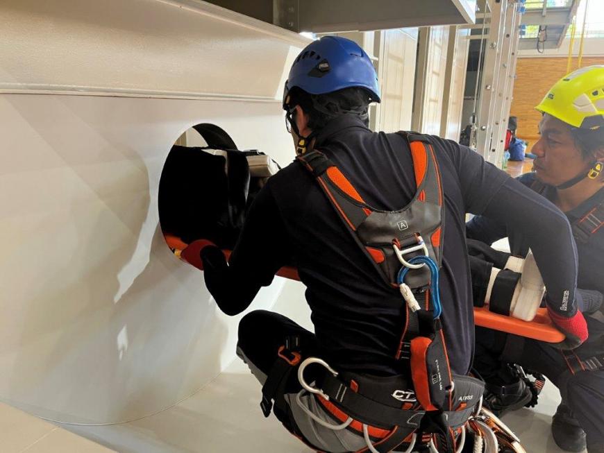 床にしゃがみ、壁に空いている丸い穴の中に道具を使って入れようとしている様子の実習の写真