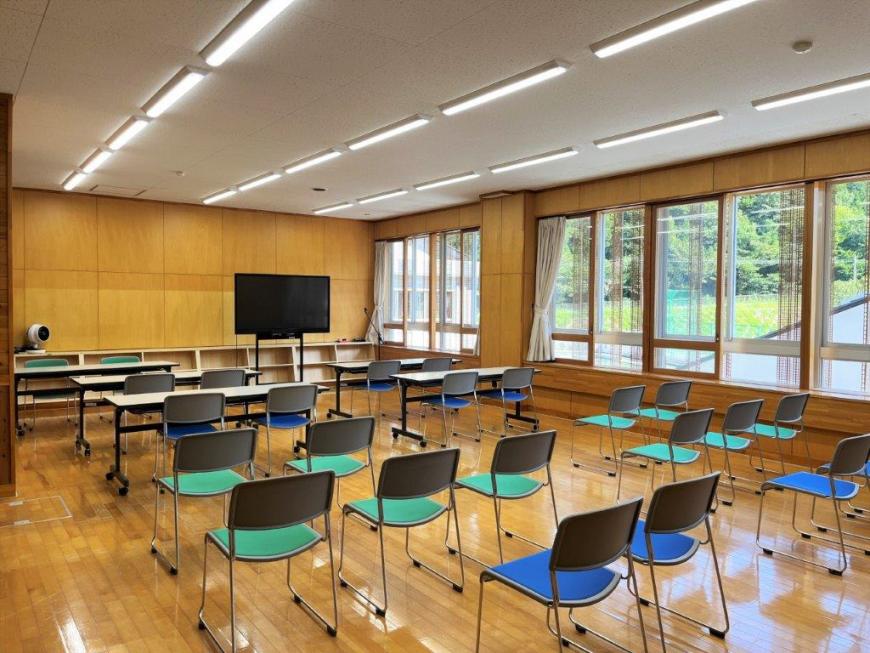 前方にモニターがあり長机や椅子が並べられた研修室の写真