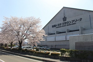満開の桜の木の後ろに立っている三角屋根の福島トヨタクラウンアリーナの写真