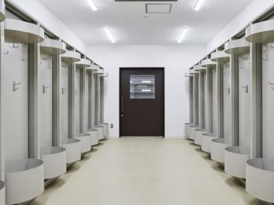 中央奥に茶色の扉の出入り口があり、左右に荷物置きや4か所ずつフックが設置された室内の写真