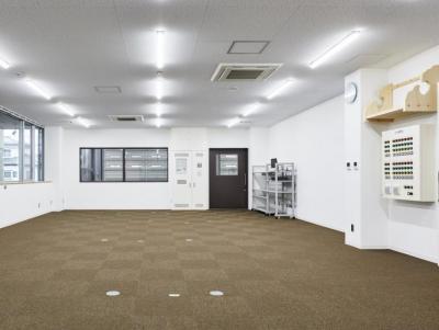 右奥に茶色の扉、左側に窓があり、床には茶色の絨毯が敷き詰められ、右側に神棚が設置された室内の写真