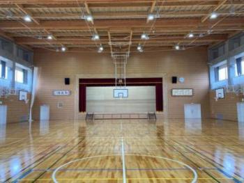 奥にステージがあり左右にバスケットゴールが設置された、床がピカピカに光っている体育館内の写真
