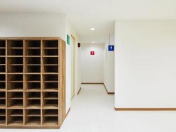 左側に靴箱が設置された通路の左側に緑色の看板、右側に青色の看板、奥の壁に赤色の看板が設置されたトイレの入口付近の写真