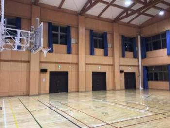 ベージュ色の壁で窓ガラスに青色のカーテンが設置された体育館の写真