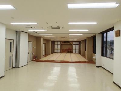 左側に出入り口の扉、右側に窓ガラスが設置され、奥に畳敷きのスペースがある室内の写真