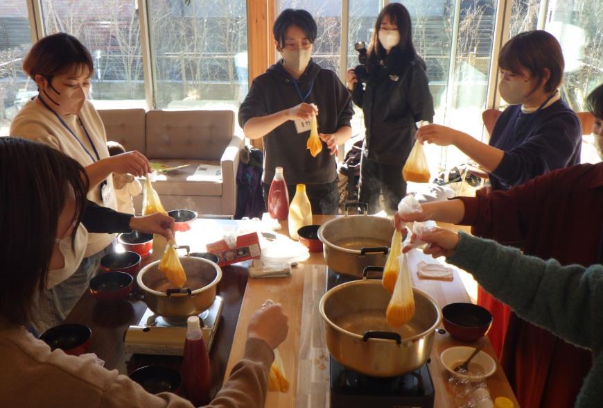 参加者の皆さんがビニール袋の中に卵液を入れ、コンロの上の鍋に卵液をいれようとしている「焼かないオムレツ」の調理の様子の写真