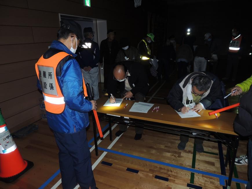 暗闇の中、長机が設置された場所で、ペンライトで光を照らしながら、受付をしている様子の写真