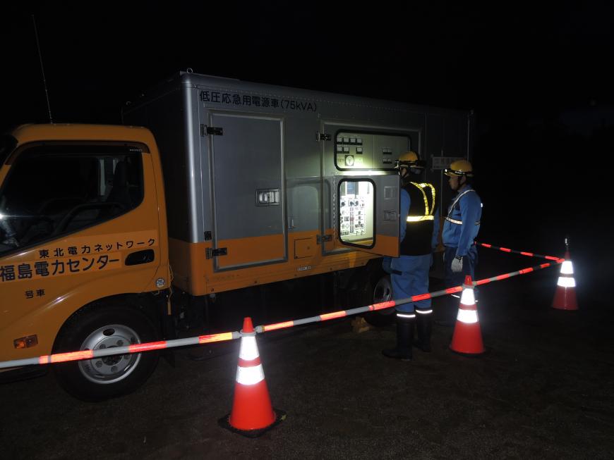 暗闇の中低圧応急用電源車の荷台部分にある機械の扉をあけ、2名の関係者が作業をしている様子の写真