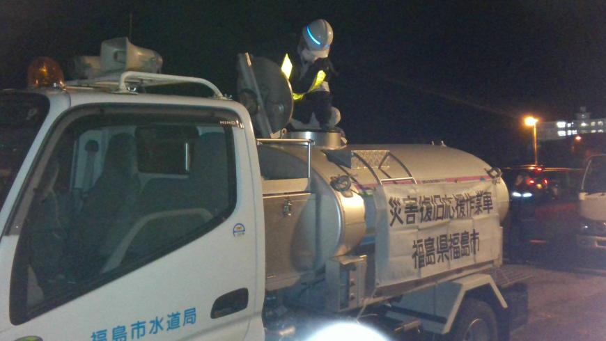 「災害復旧応援作業車 福島県福島市」と書かれた横断幕がつけられた給水車の上で男性が作業をしている給水支援の様子の写真