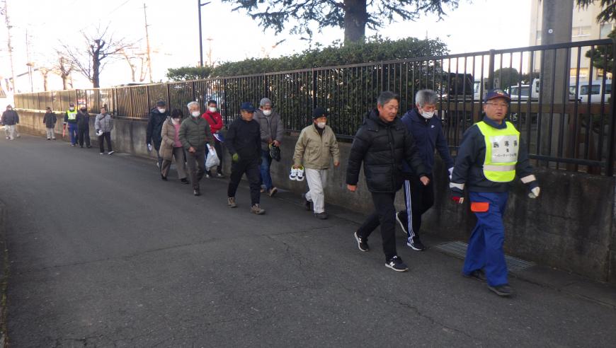 地元住民の方々が道路の端を黄色いビブスをつけた男性の後に続いて1列に並び歩いている様子を写した写真