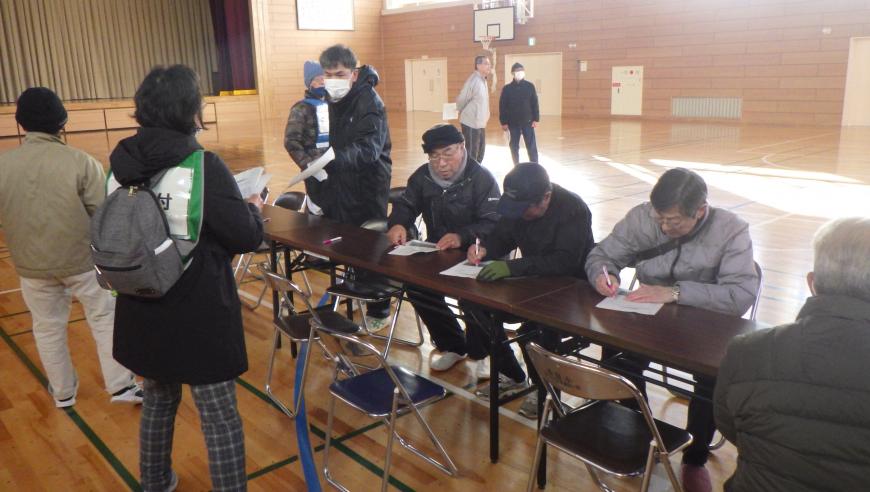 体育館内に長机が設置され、関係者の方々が座って書類に記載している様子を写した写真