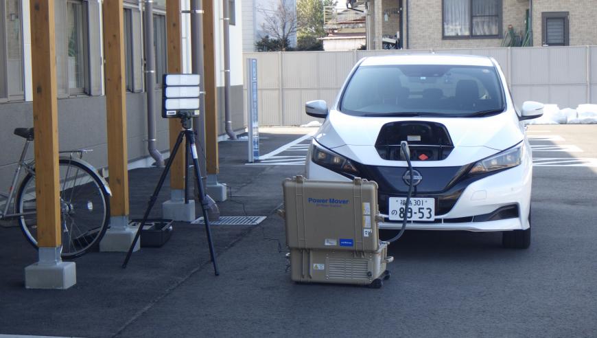 電気自動車の車体の前にある充電口からケーブルを箱型の機械につなぎ、電源確保を行っている様子の写真