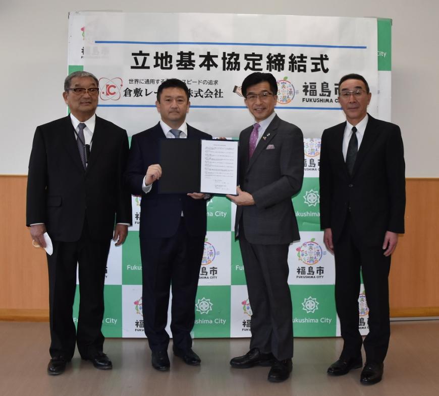 立地基本協定締結式と書かれたバックパネルの前で、難波社長と市長が一緒に協定書を持ち、両端に難波会長と松川支所長が横一列に並んでいる写真