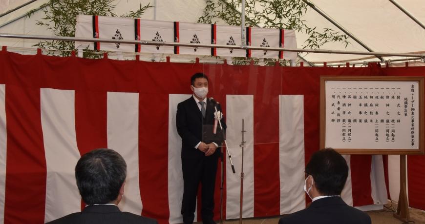 紅白幕が貼られた地鎮祭の式の会場で、難波社長がスタンドマイクの前に立ち挨拶を行っている様子の写真