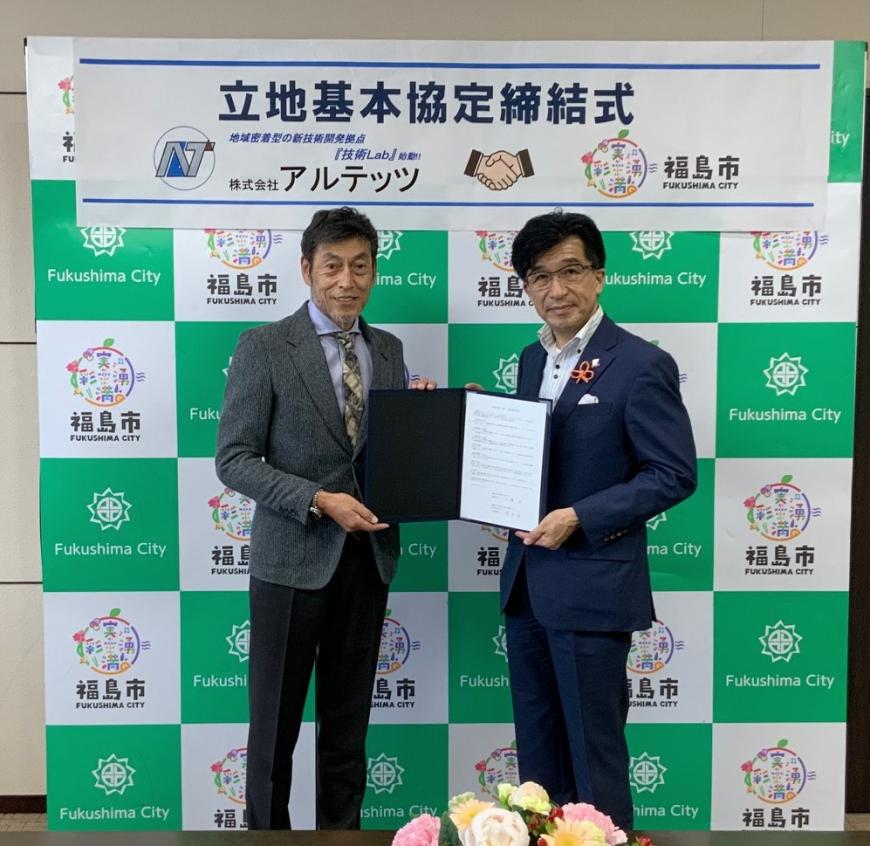 立地基本協定締結式と書かれたバックパネルの前で、櫻井代表取締役と市長が一緒に協定書を持ち並んでいる写真