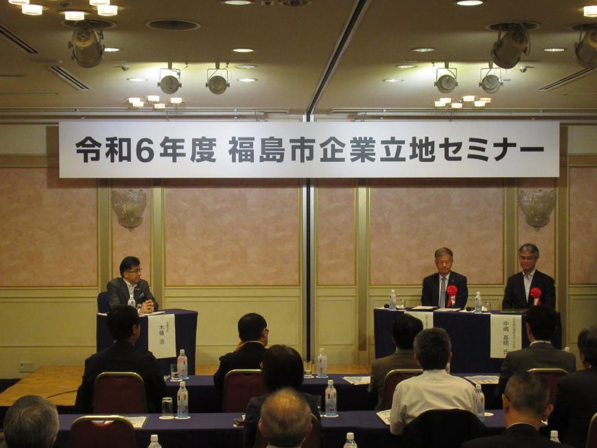 「令和6年度福島市企業立地セミナー」と書かれた横断幕が掲げられた会場の左側に市長が座り、右側に小形氏と中嶋氏が座ってトークセッションが行われている様子の写真