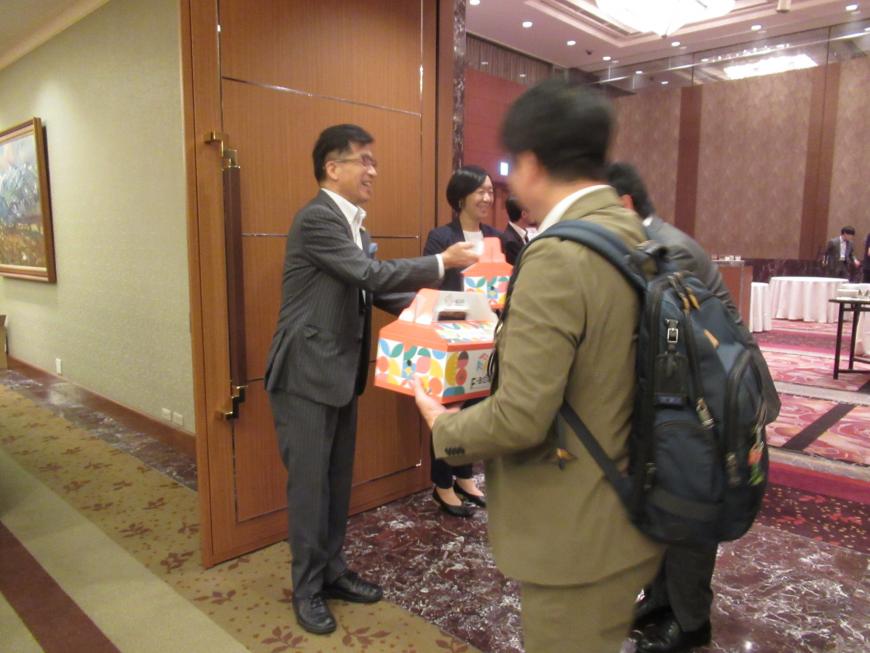セミナー終了後に会場の出口付近で担当者から参加者たちに箱入りのお土産が配られている様子の写真