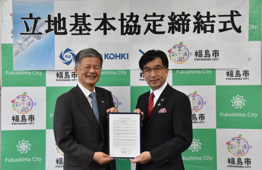 立地基本協定締結式と書かれたバックパネルの前で、小形社長と市長が一緒に協定書を持ち並んでいる写真