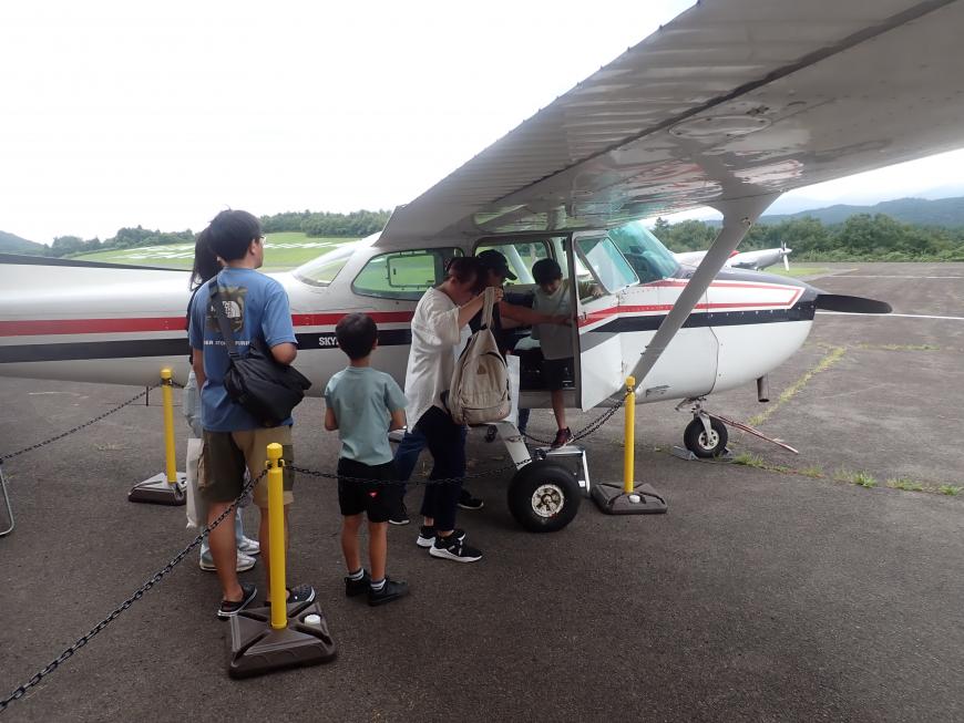 親子連れで参加した子供たちが、小型飛行機のコックピット見学を行っている様子の写真