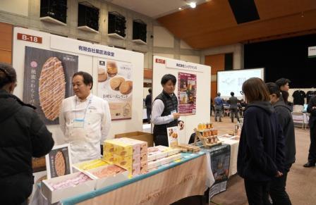 ポスターが展示されお菓子の商品が並んだブースに2名の女性が興味深そうに見ている写真