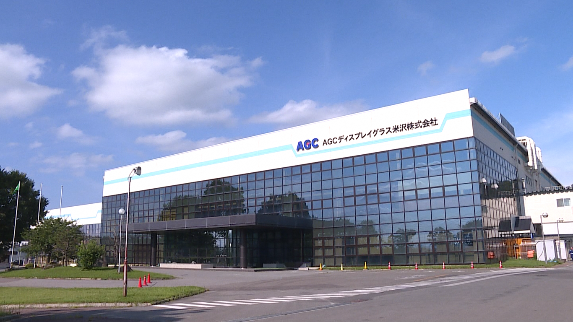 上部に水色のラインの上にAGCディスプレイグラス米沢株式会社と書かれたガラス張りの建物外観の写真