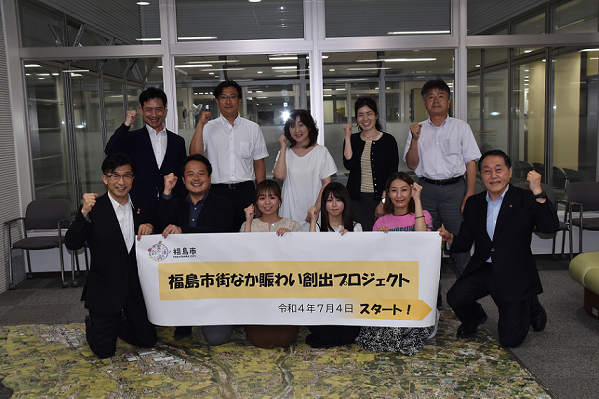 福島市街なか賑わい創出プロジェクト 令和4年7月4日スタート!の横断幕を持ち、関係者11名がガッツポーズをして記念撮影をしている写真