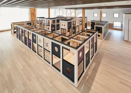 正方形に組まれた木枠を沢山積み重ねたり並べたりして作られた屋内こども遊び場の木製遊具の写真