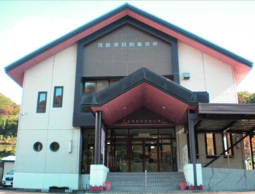 三角屋根で壁に「茂庭多目的集会所」と書かれた2階建ての建物外観の写真