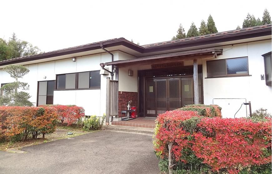 建物の入り口前の左右に手入れが行き届いた植木があり、白壁で平屋の立子山多目的集会所の建物外観の写真
