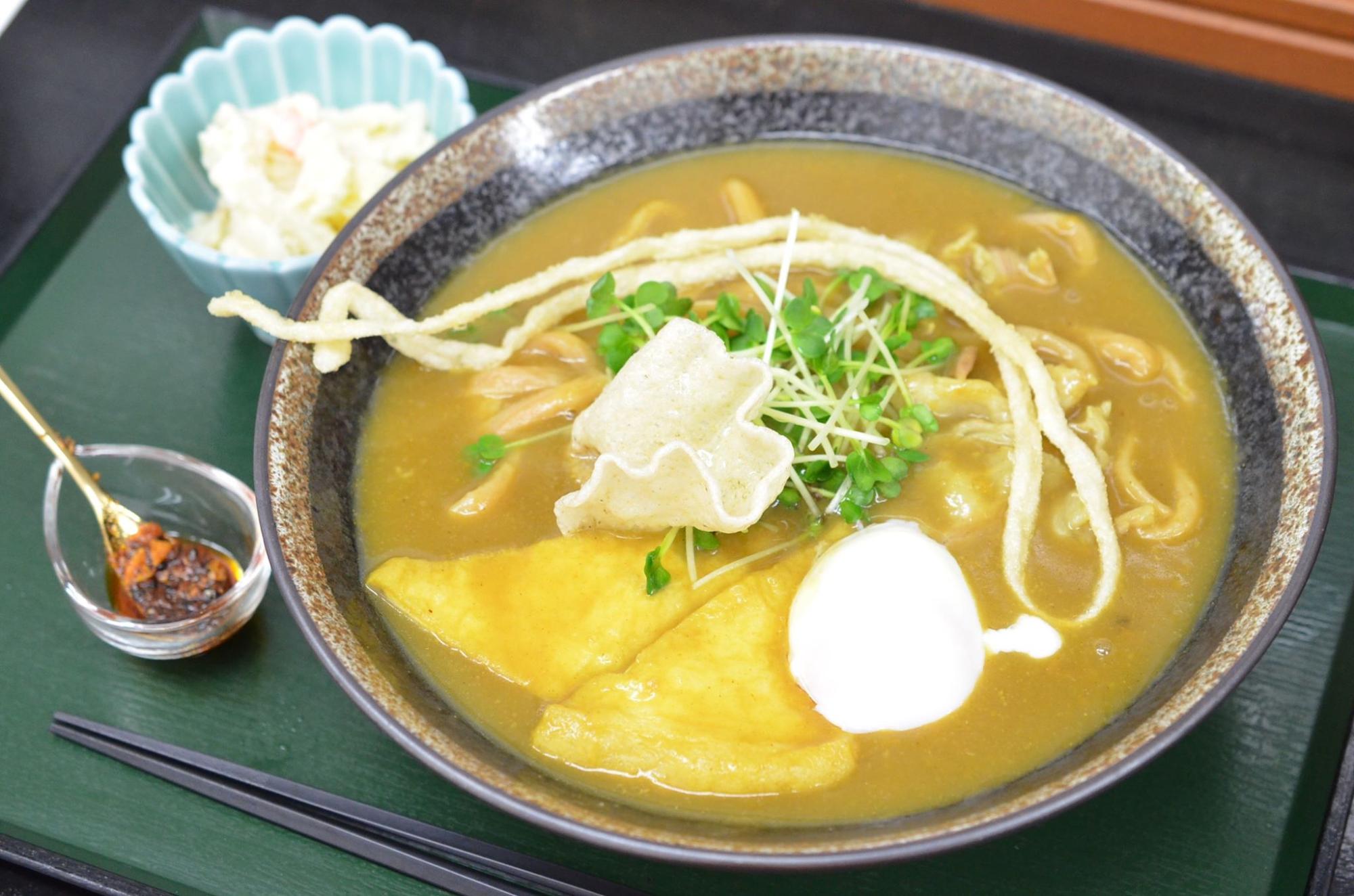 トレイの上に小鉢に入った副菜と、大きな丼に具沢山のカレーうどんが盛り付けられた写真