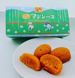 かぼちゃ畑での収穫の様子が描かれた箱と、白い丸皿に盛り付けられた2つのオレンジ色の雪っ娘マドレーヌと半分にカットされたマドレーヌの写真