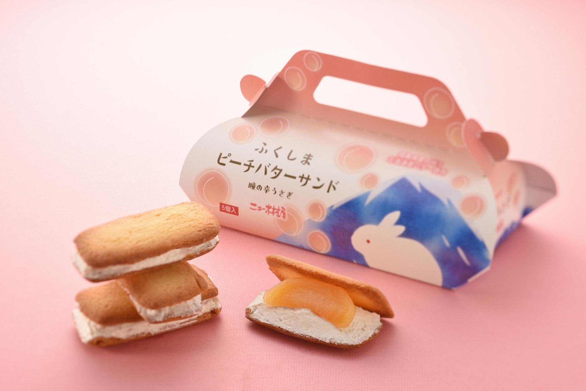 雪がつもった山とウサギのイラストが描かれ「ふくしまピーチバターサンド」と書かれた箱の前に置かれた、大きな白桃とクリームがが2枚のビスケットでサンドされた商品の写真