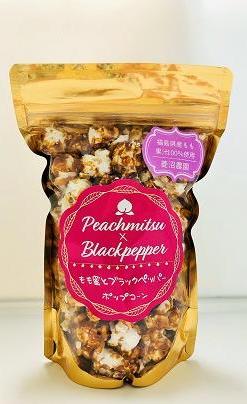 金色で正面が透明な袋の中央に「もも蜜とブラックペッパー」と書かれた濃いピンク色のラベルが貼られたポップコーンの写真