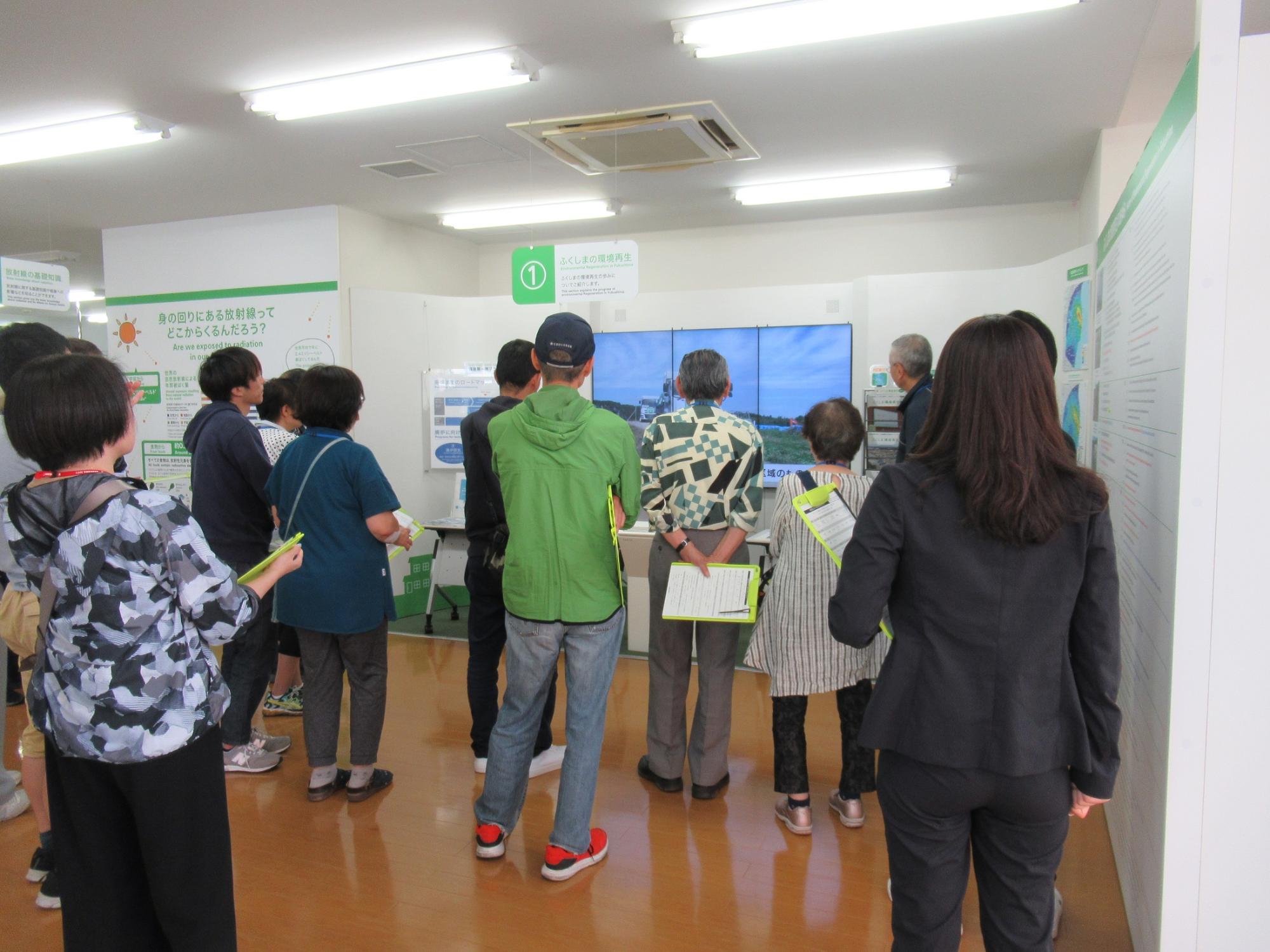 冊子を手にした参加者たちが壁の展示を見ている写真