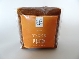 透明のパッケージににオレンジ色地に白文字で「てづくり味噌」と書かれた商品の写真