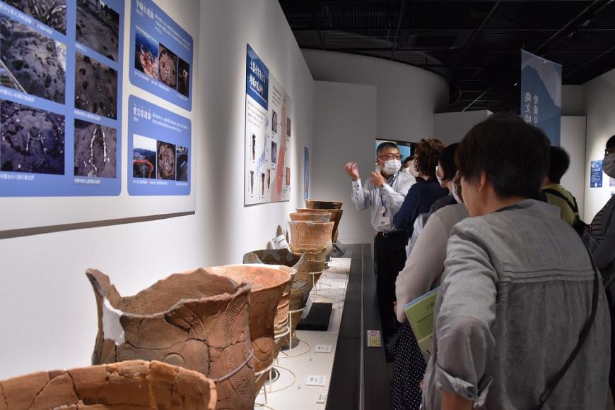 展示されている土器を見ながら係の方の説明を聞いている参加者の方々の写真