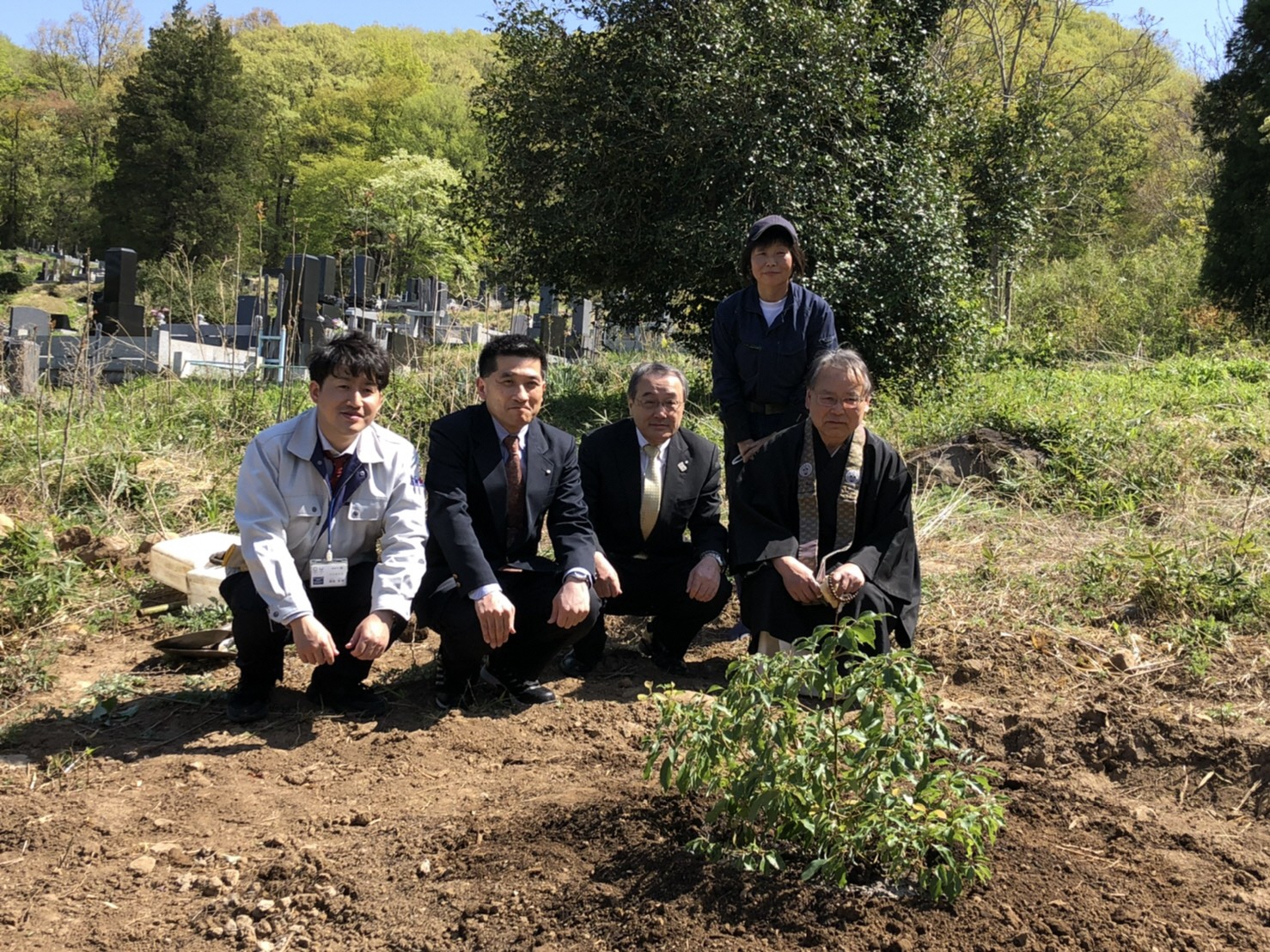 植樹したクスノキの前で関係者5名が記念写真を撮影した写真
