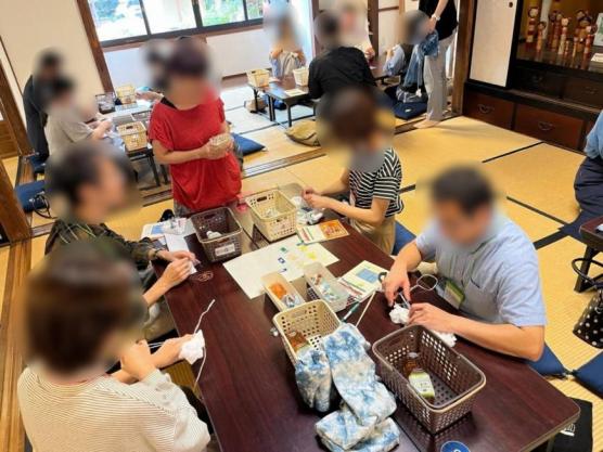 畳の部屋に設置された机に分かれ、イベントに参加した男女が藍染めをする様子の写真