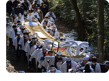 白いハチマキと法被を着た参加者達が大わらじを担いで信夫山を上る様子の写真
