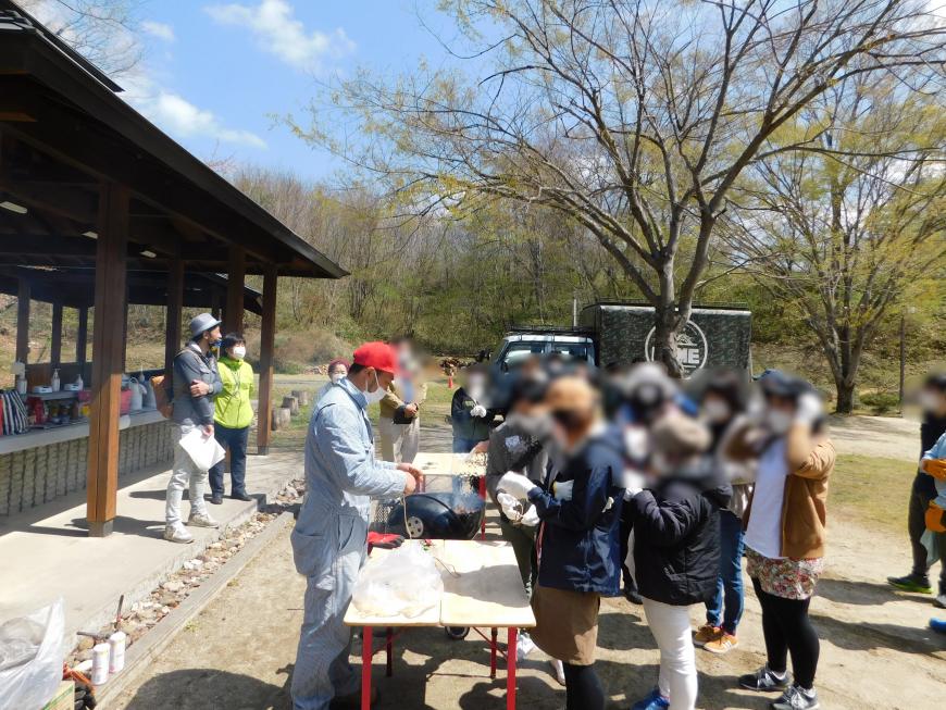 前で関係者が話をしているのを参加者達が聞いている様子の写真