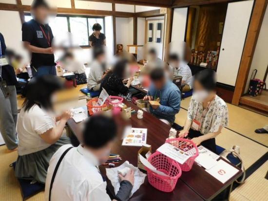 参加者達がテーブルごとのグループに分かれて「まねきねこ」の絵付け体験をする様子の写真