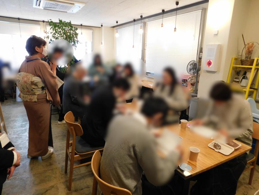 参加者達が2人1組のテーブルに分かれ食事をする様子の写真