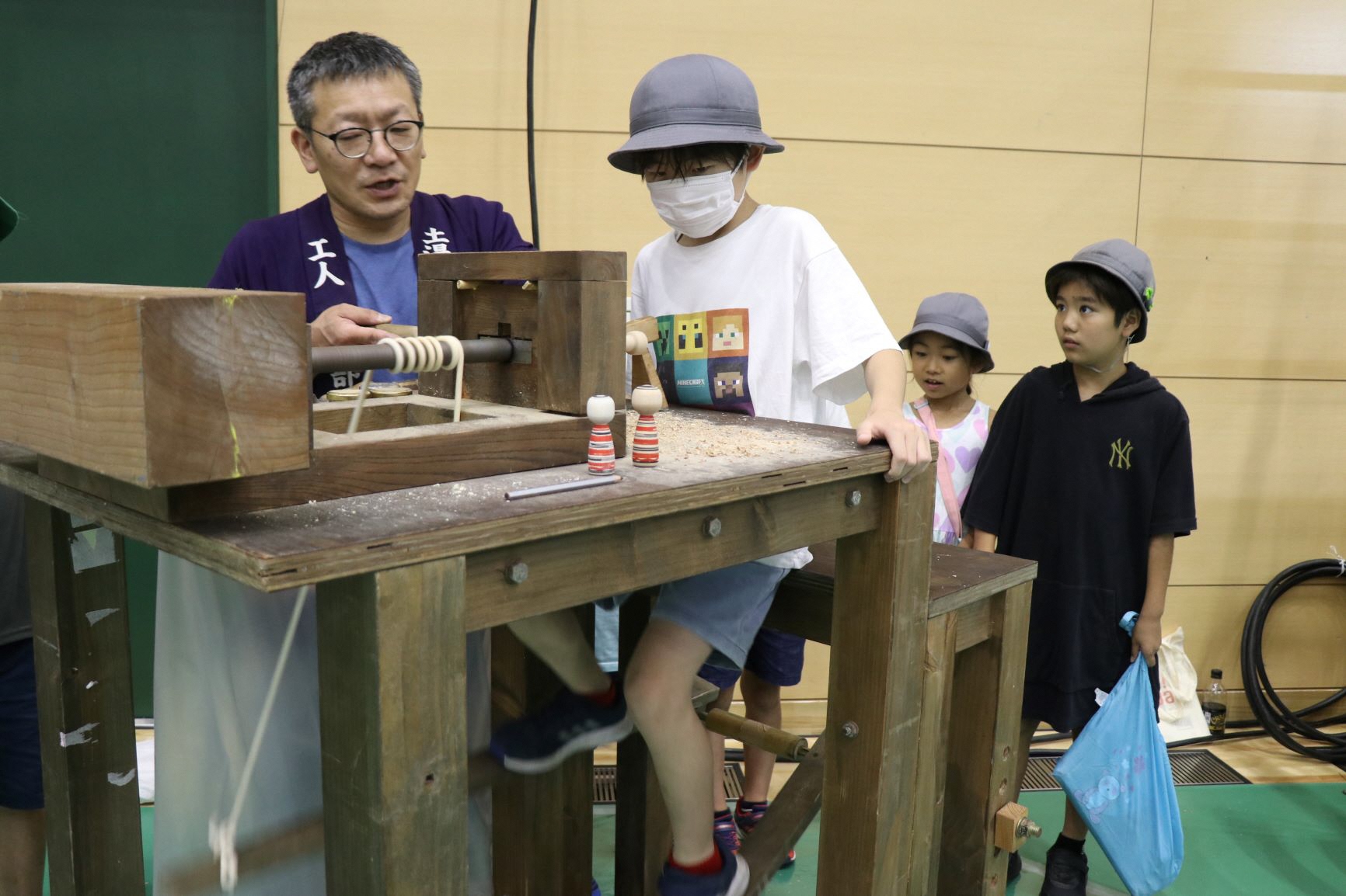 紫色の法被を着た男性の指導のもと男の子が機械の前に座り体験をする様子の写真