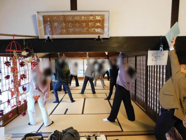 二間続きの和室に参加者達が並び左手を上に伸ばしヨガを行っている様子の写真