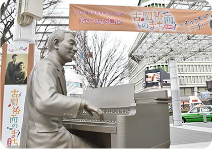 「「エール」の舞台古関裕而のまち」と書かれた横断幕が掲げられた駅前に建てられた古関裕而のモニュメントの写真