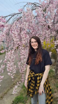 桃色に咲いた枝垂れ桜の前に立っているサマンサ・バーネットさんの写真